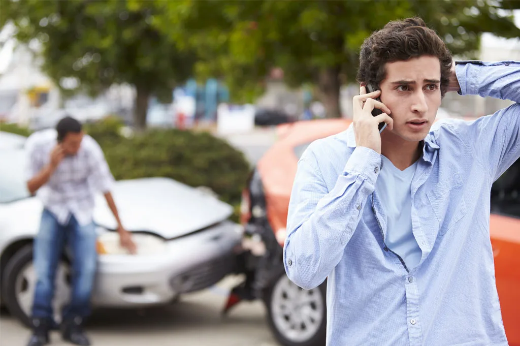A young man on the phone calling a personal injury attorney while is on the scene of a car accident